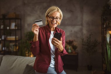 Olgun yaşlı kadın cep telefonundan satın alır ve kredi kartı kullanır.