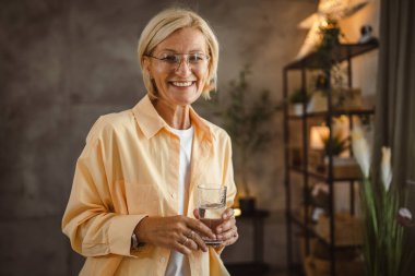 Güzel olgun yaşlı bir kadının portresi otur ve elinde bir bardak su tut.