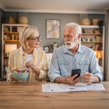 Üst düzey çift kağıt faturaları ve faturaları okurken ve ödemeler hakkında tartışırken kadın karısı salata yiyor.