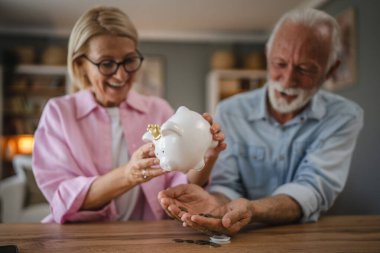Yaşlı çift domuz kumbarasından para sayıyor ve birlikte para biriktiriyorlar.