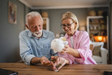 Yaşlı çift domuz kumbarasından para sayıyor ve birlikte para biriktiriyorlar.