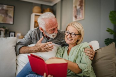 Olgun bir eş kanepeye uzanır kitap okur ve kıdemli kocasıyla bu konuyu tartışır.