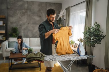 Yetişkin adam, kadın tozları temizlerken gardırobu demir tahtada ütülüyor.