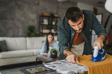 Yetişkin adam, kadın tozları temizlerken gardırobu demir tahtada ütülüyor.