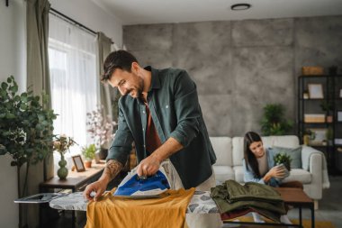 Yetişkin adam, kadın tozları temizlerken gardırobu demir tahtada ütülüyor.