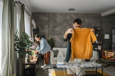 Yetişkin adam, kadın tozları temizlerken gardırobu demir tahtada ütülüyor.