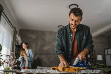 Yetişkin adam, kadın tozları temizlerken gardırobu demir tahtada ütülüyor.