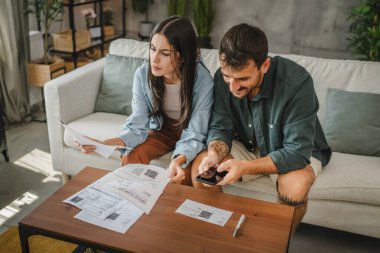 Yetişkin bir adamın cep telefonunda, kız arkadaşı kanepede onun yanında otururken ödeme faturası var.