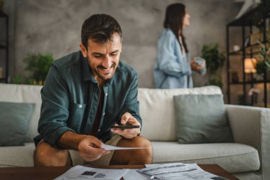 Yetişkin adam faturaları kontrol ediyor ve cep telefonundan ulaşılamayan bir ödeme alıyor.