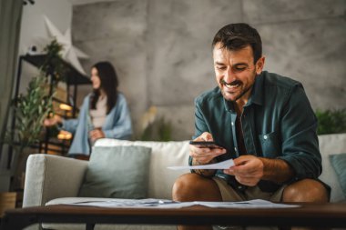 Yetişkin adam faturaları kontrol ediyor ve cep telefonundan ulaşılamayan bir ödeme alıyor.