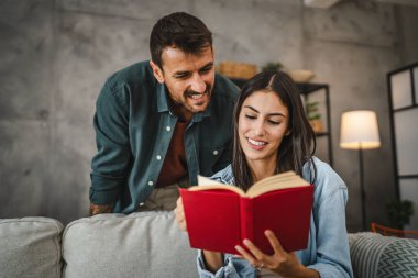 Kız arkadaşım kanepeye oturup kitap okurken erkek arkadaşım ona sarılıyor.