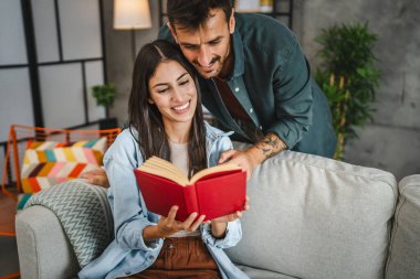 Kız arkadaşım kanepeye oturup kitap okurken erkek arkadaşım ona sarılıyor.