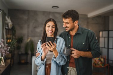 Kız arkadaşının portresi, erkek arkadaşı evde kahve içerken ona cep telefonu ekranını gösteriyor.
