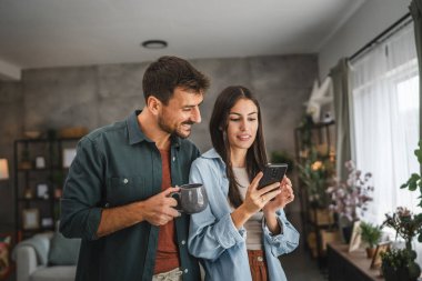 Kız arkadaşının portresi, erkek arkadaşı evde kahve içerken ona cep telefonu ekranını gösteriyor.
