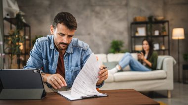 Yetişkin adam evde çalışıyor. Belge okuyor, sigorta yaptırıyor.