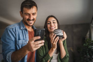 Sevgilisi evde kahve içerken ona cep telefonu ekranını göster.