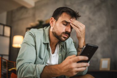 Öfkeli yetişkin bir adamın portresi sandalyeye oturup cep telefonuna mesaj atıyor.