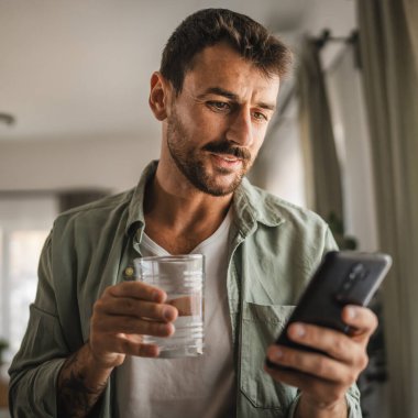 Yetişkin erkeklerin portresi bir bardak su ve cep telefonu taşıyor.