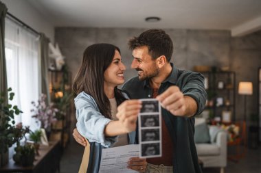 Yetişkin çift ayağa kalkar ve bebeğin ve tıbbi belgelerin ultrason fotoğrafını tutar.