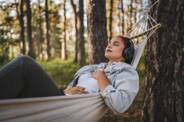 Kulaklıklı genç kadın hamakta uzanıyor ve dağda meditasyona rehberlik ediyor.