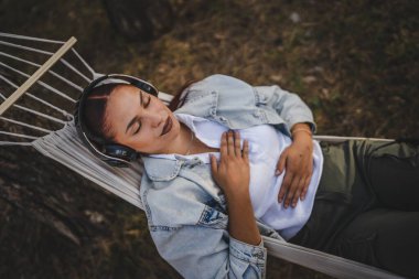 Kulaklıklı genç kadın hamakta uzanıyor ve dağda meditasyona rehberlik ediyor.
