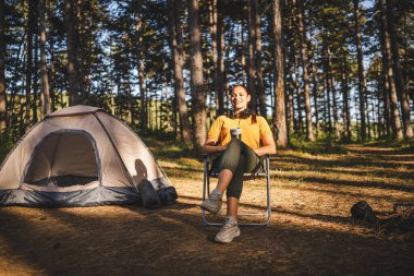 Genç bayan çadırın önünde oturup termosta kahve içiyor.