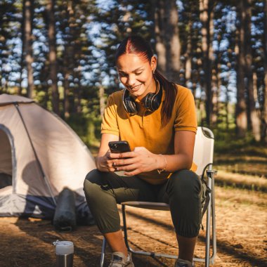 Genç bayan çadırın önünde oturuyor ve dağda, ormanda cep telefonu kullanıyor.