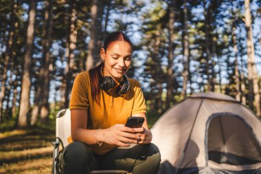 Genç bayan çadırın önünde oturuyor ve dağda, ormanda cep telefonu kullanıyor.