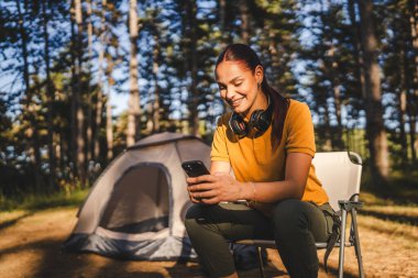 Genç bayan çadırın önünde oturuyor ve dağda, ormanda cep telefonu kullanıyor.
