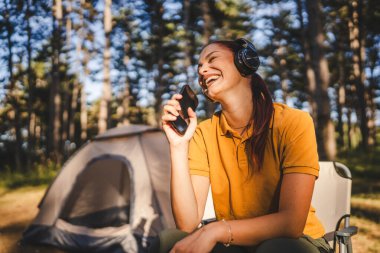 Kulaklıklı genç bir kadın önde oturur müzik dinler ve cep telefonuyla şarkı söyler.