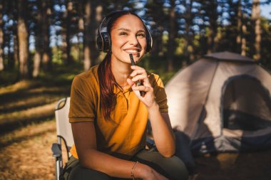 Kulaklıklı genç bir kadın önde oturur müzik dinler ve cep telefonuyla şarkı söyler.