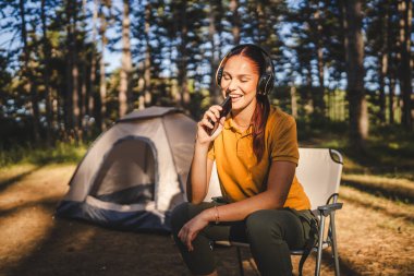 Kulaklıklı genç bir kadın önde oturur müzik dinler ve cep telefonuyla şarkı söyler.