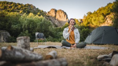 Genç kadın bacak bacak üstüne atmış bir şekilde battaniyeye oturur kulaklıklarla müzik dinler ve cep telefonuyla şarkı söylerdi.