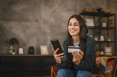 Yetişkin kadınlar evlerinde cep telefonlarıyla internet üzerinden alışveriş yaparlar.