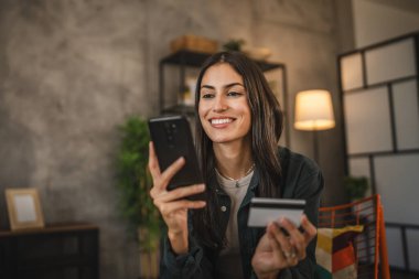 Yetişkin kadınlar evlerinde cep telefonlarıyla internet üzerinden alışveriş yaparlar.