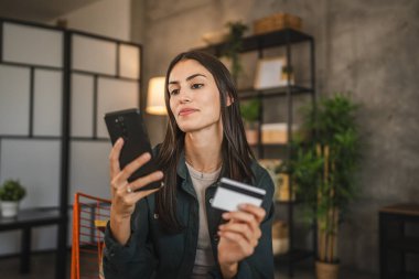Yetişkin kadınlar evlerinde cep telefonlarıyla internet üzerinden alışveriş yaparlar.