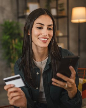 Yetişkin kadınlar evlerinde cep telefonlarıyla internet üzerinden alışveriş yaparlar.
