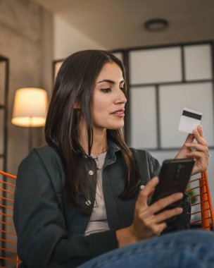 Yetişkin kadınlar evlerinde cep telefonlarıyla internet üzerinden alışveriş yaparlar.