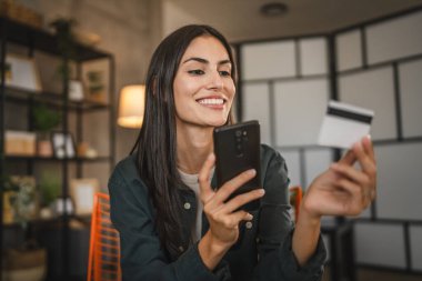 Yetişkin kadınlar evlerinde cep telefonlarıyla internet üzerinden alışveriş yaparlar.