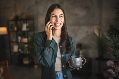 Yetişkin bir genç kadının portresi. Bardağı tut ve cep telefonuyla konuş.