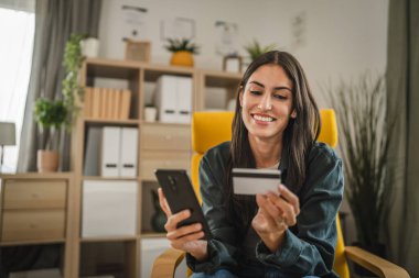 Yetişkin kadınlar evlerinde cep telefonlarıyla internet üzerinden alışveriş yaparlar.