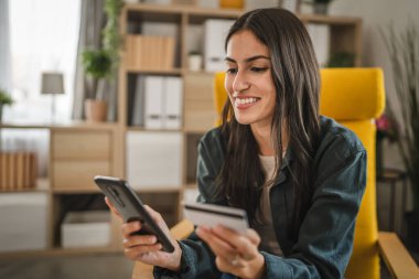 Yetişkin kadınlar evlerinde cep telefonlarıyla internet üzerinden alışveriş yaparlar.