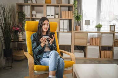 Yetişkin kadınlar evlerinde cep telefonlarıyla internet üzerinden alışveriş yaparlar.