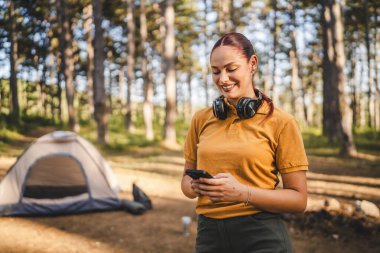 Kulaklıklı genç bir kadının portresi çadırın önünde duruyor. Cep telefonu kullan.
