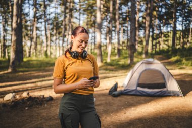 Kulaklıklı genç bir kadının portresi çadırın önünde duruyor. Cep telefonu kullan.