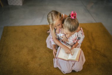 older friend sister help her young friend sister to read a book, understand part of book clipart