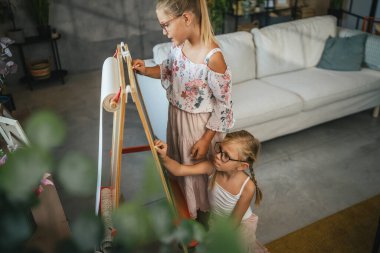 İki genç kız, kız kardeşler eğleniyor. Evdeki tahtaya yazıp çiziyorlar.