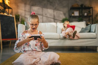 Genç beyaz kız yerde oturup cep telefonunu eğlence ve video oyunları için kullanıyor.