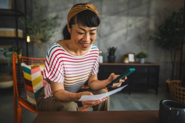 Mature japanese woman have contactless payment, scan invoice on cellphone at home clipart