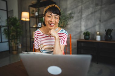 Olgun Japon kadın evde kulaklıkla çalışıyor ve laptopundan video görüşmesi yapıyor.
